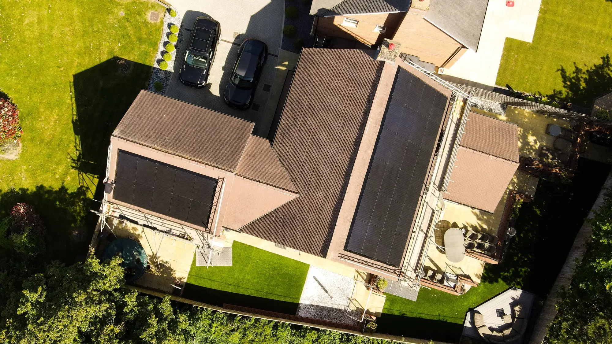 Drone photograph straight down on a brick house with two all-black solar arrays and two cars on the drive