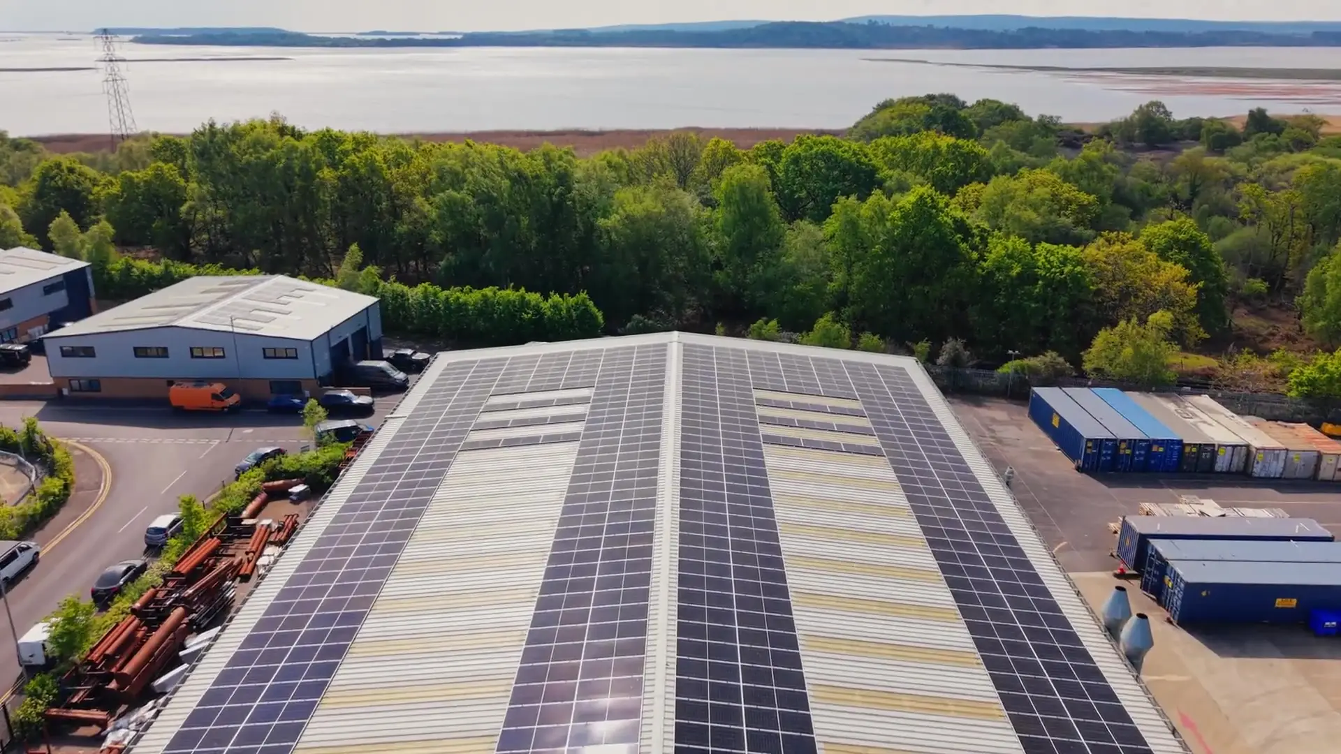 Drone view of a completed commercial solar array on a warehouse roof beside Poole Harbour