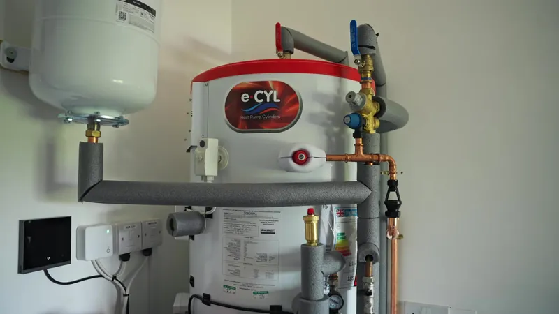 Heat pump hot water cylinder with insulated pipework and controls in a utility room