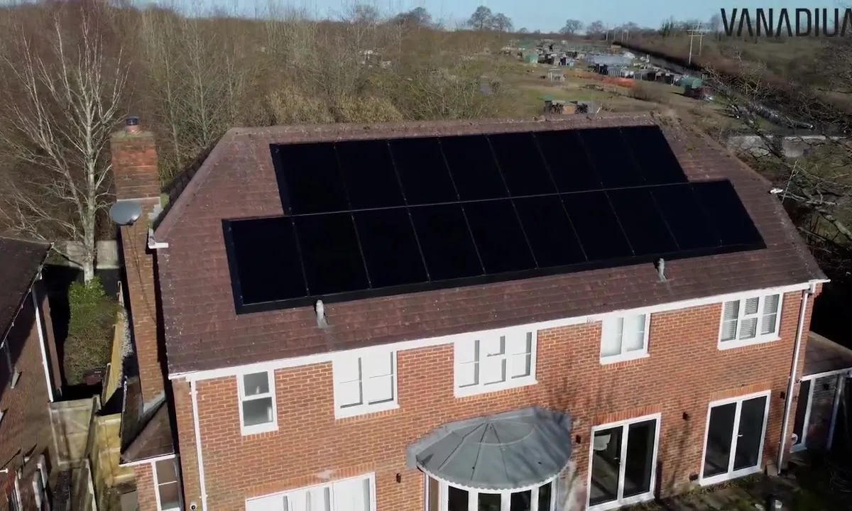 Aerial view of a red brick house with black solar panels on the roof.