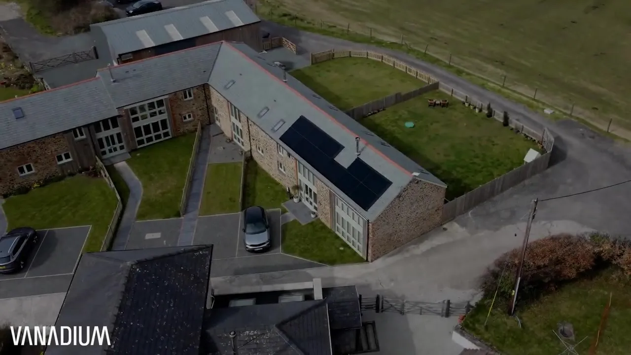 Aerial view of a barn conversion in Devon with black solar panels on the roof and an electric car parked outside.