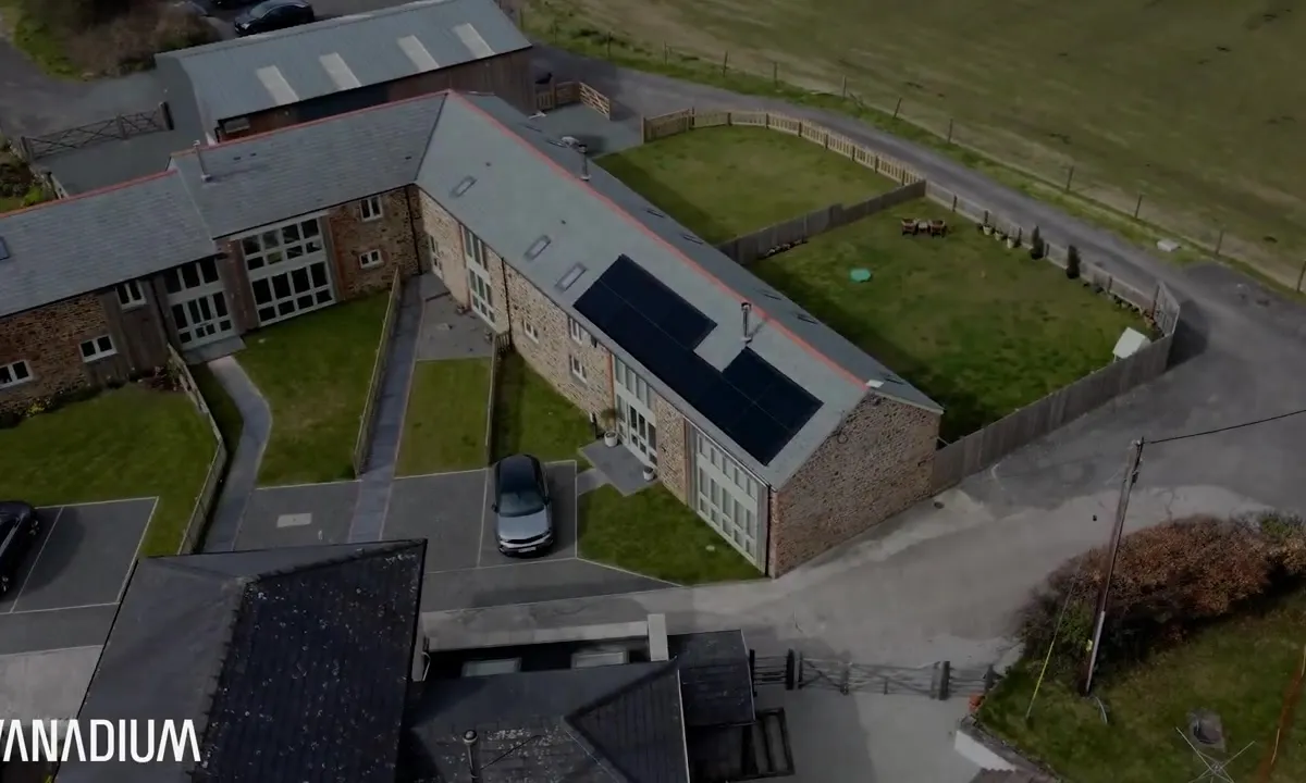 Aerial view of a barn conversion in Devon with black solar panels on the roof and an electric car parked outside.