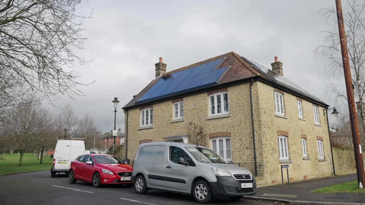 Stone house with solar panels on the roof and cars parked outside.