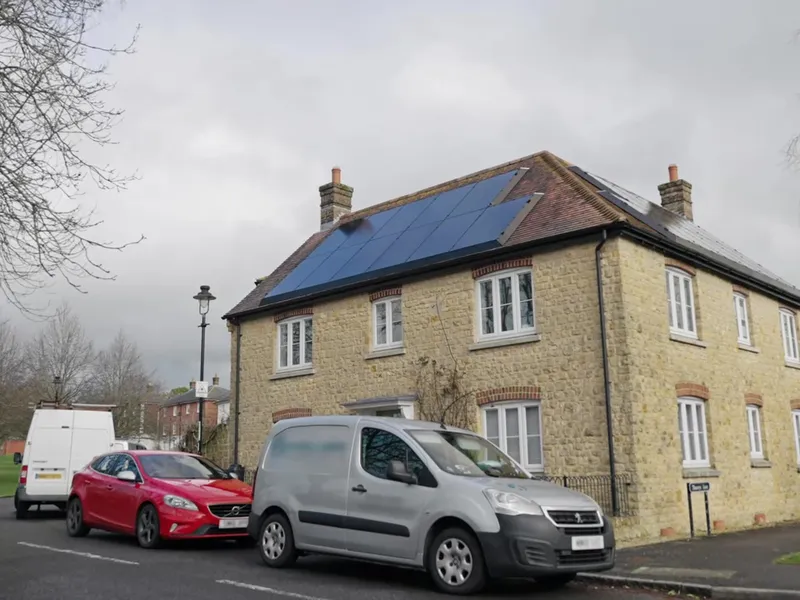 Stone house with solar panels on the roof and cars parked outside.