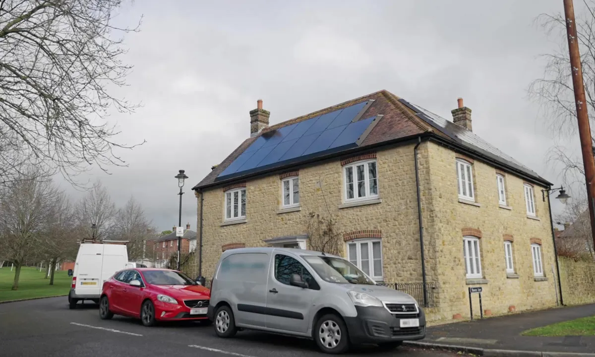 Stone house with solar panels on the roof and cars parked outside.