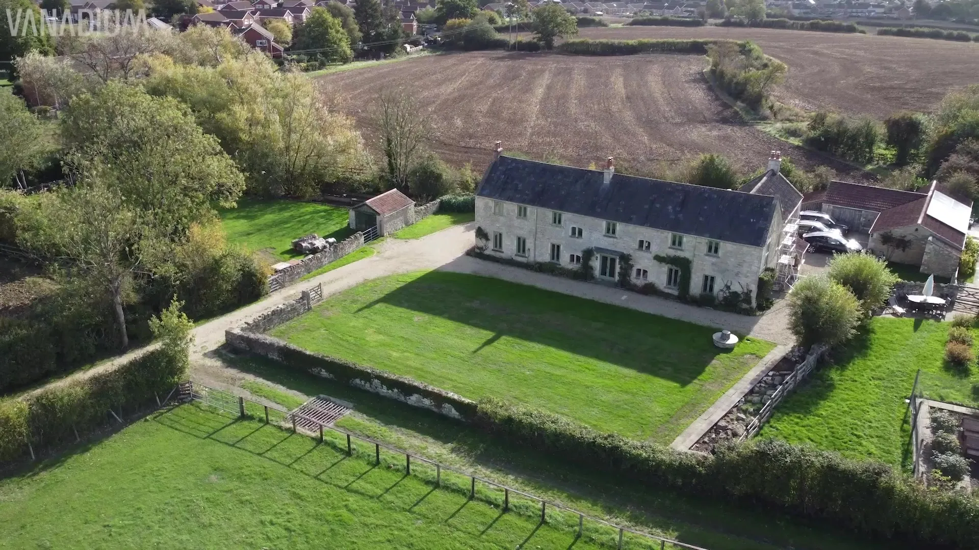 Aerial view of a large stone house, green fields, and ground-mounted solar panels in Dorset.