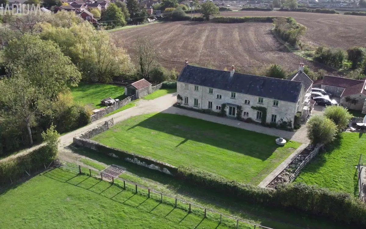 Aerial view of a large stone house, green fields, and ground-mounted solar panels in Dorset.