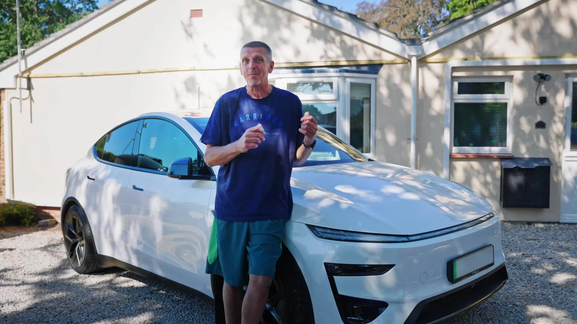The homeowner standing in front of his white Tesla car and house with solar panels on the roof.