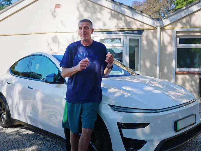 The homeowner standing in front of his white Tesla car and house with solar panels on the roof.