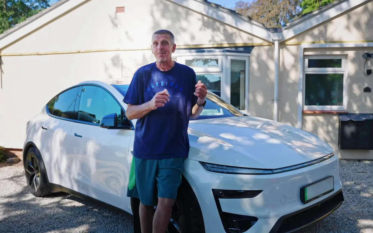 The homeowner standing in front of his white Tesla car and house with solar panels on the roof.