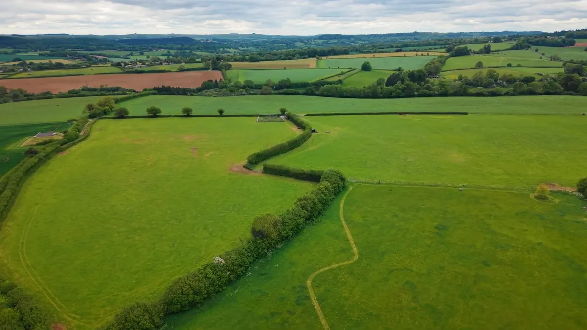 Aerial view of a green rural landscape with a farm building featuring solar panels.