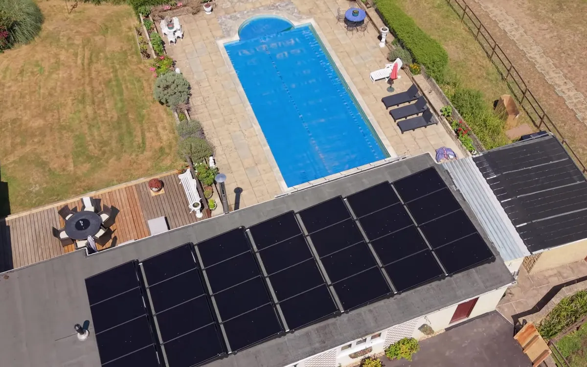 Aerial view of a bungalow with solar panels on the flat roof and a swimming pool in the garden.