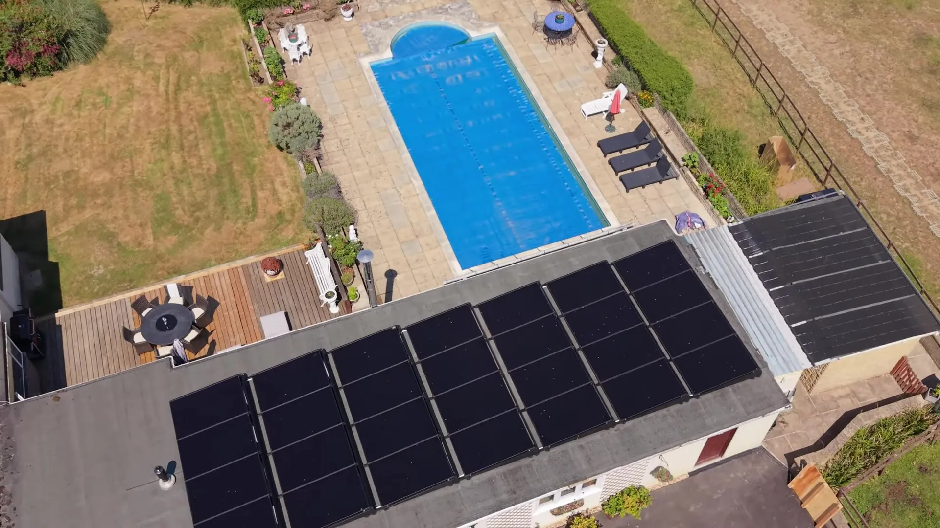 Aerial view of a bungalow with solar panels on the flat roof and a swimming pool in the garden.