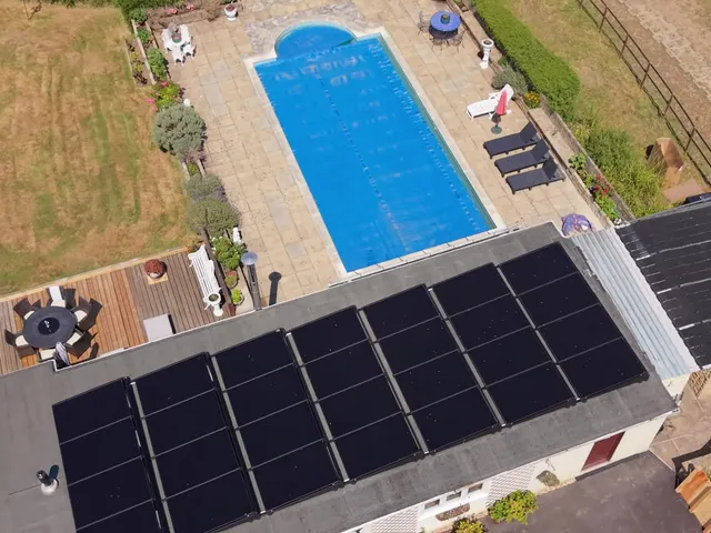 Aerial view of a bungalow with solar panels on the flat roof and a swimming pool in the garden.