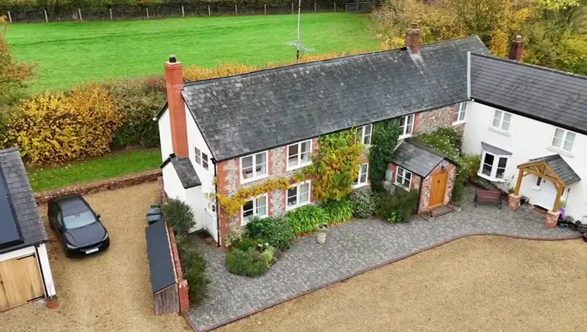 Aerial view of a rural home with a garage featuring 18 black solar panels on its roof.