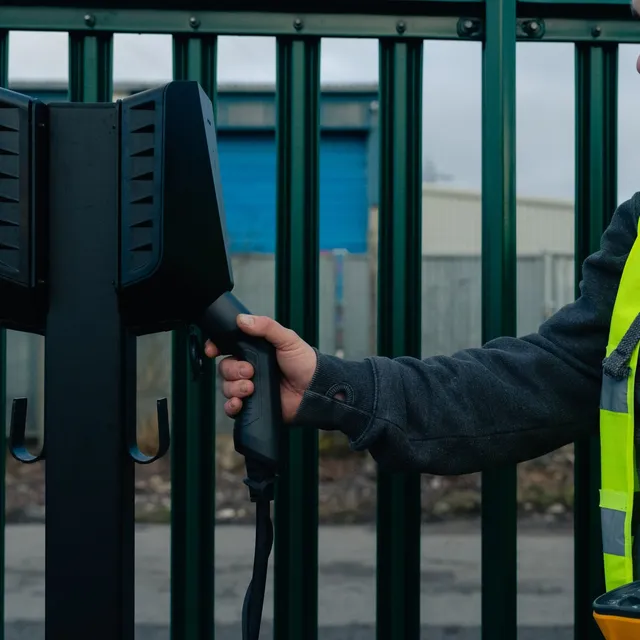 Engineer plugging a charging cable into a twin pedestal charger at a depot gate