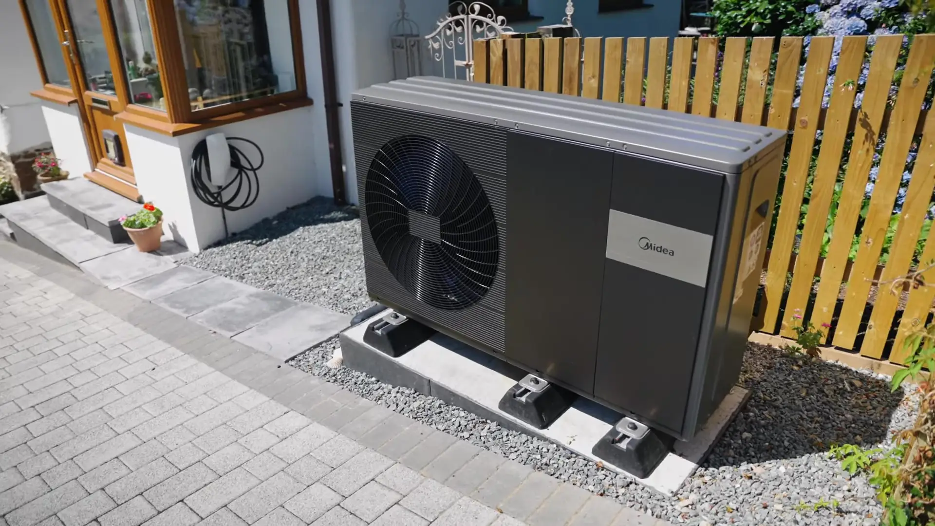 Midea air source heat pump on a gravel bed beside a cottage