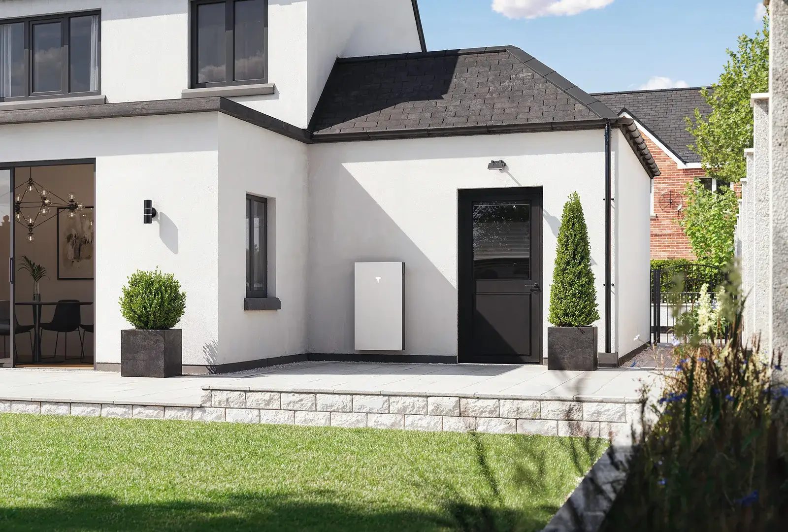 White rendered house with black solar panels on the roof and a Tesla Powerwall 3 on the wall