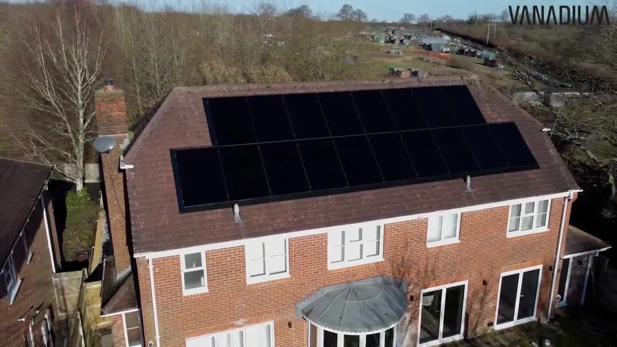 Aerial view of a red brick house with black solar panels on the roof.