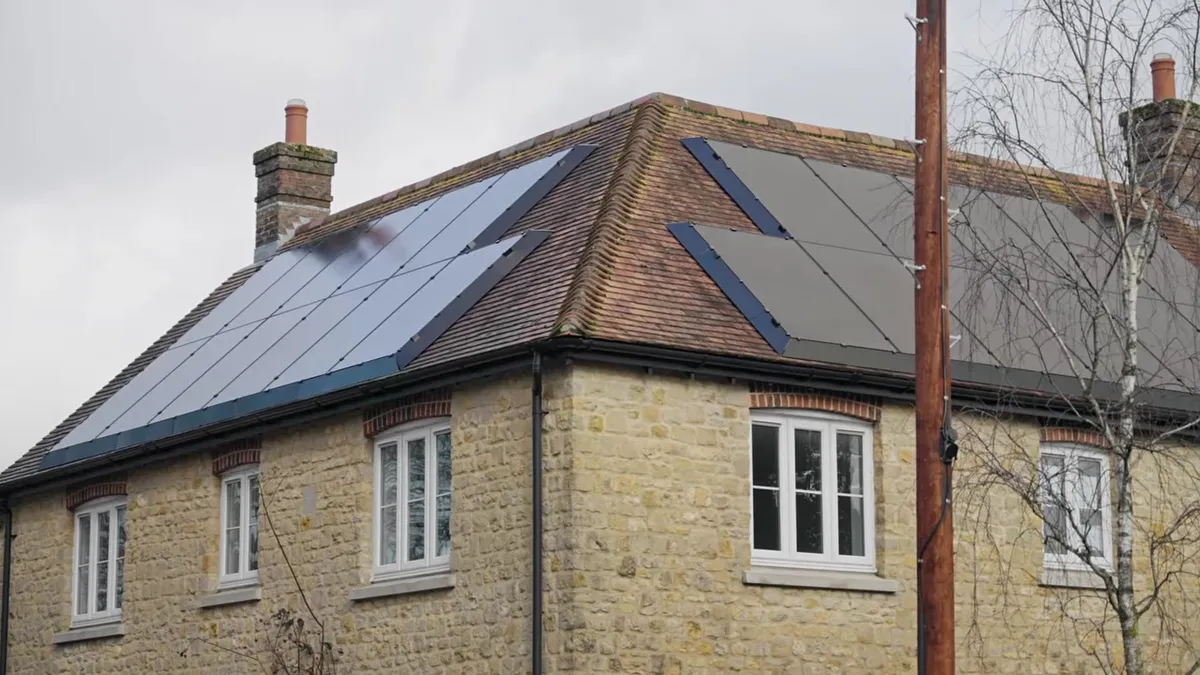 Solar panels are installed on the roof of a stone house with multiple windows.