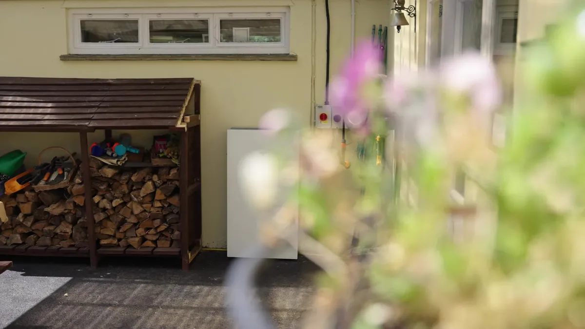 Tesla Powerwall battery unit installed on an exterior wall next to a wood store.