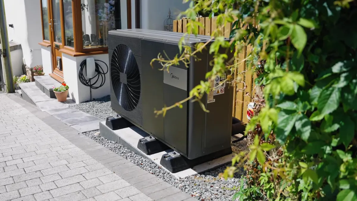 An outdoor heat pump unit is installed next to a house with an EV charger.