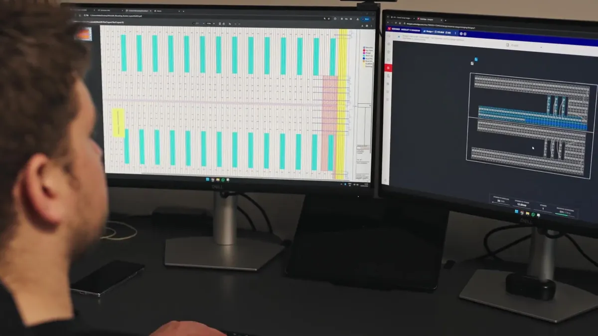 An engineer works at a desk with two computer monitors displaying solar panel layouts.