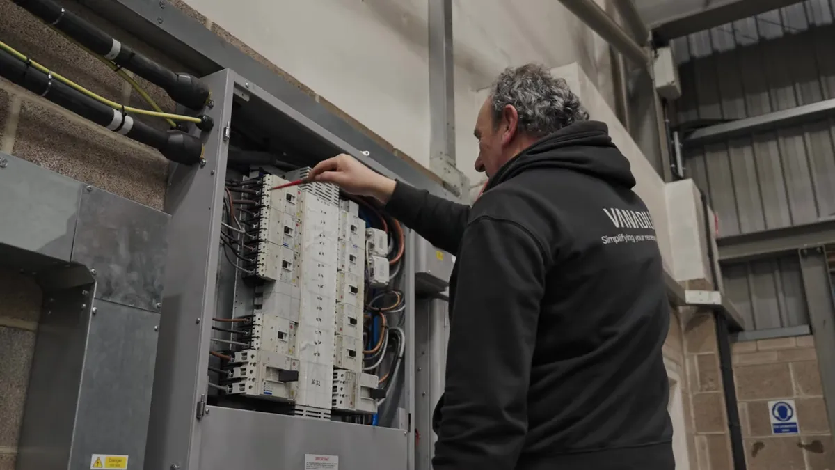 An engineer works on an electrical panel with circuit breakers and wiring in a building.