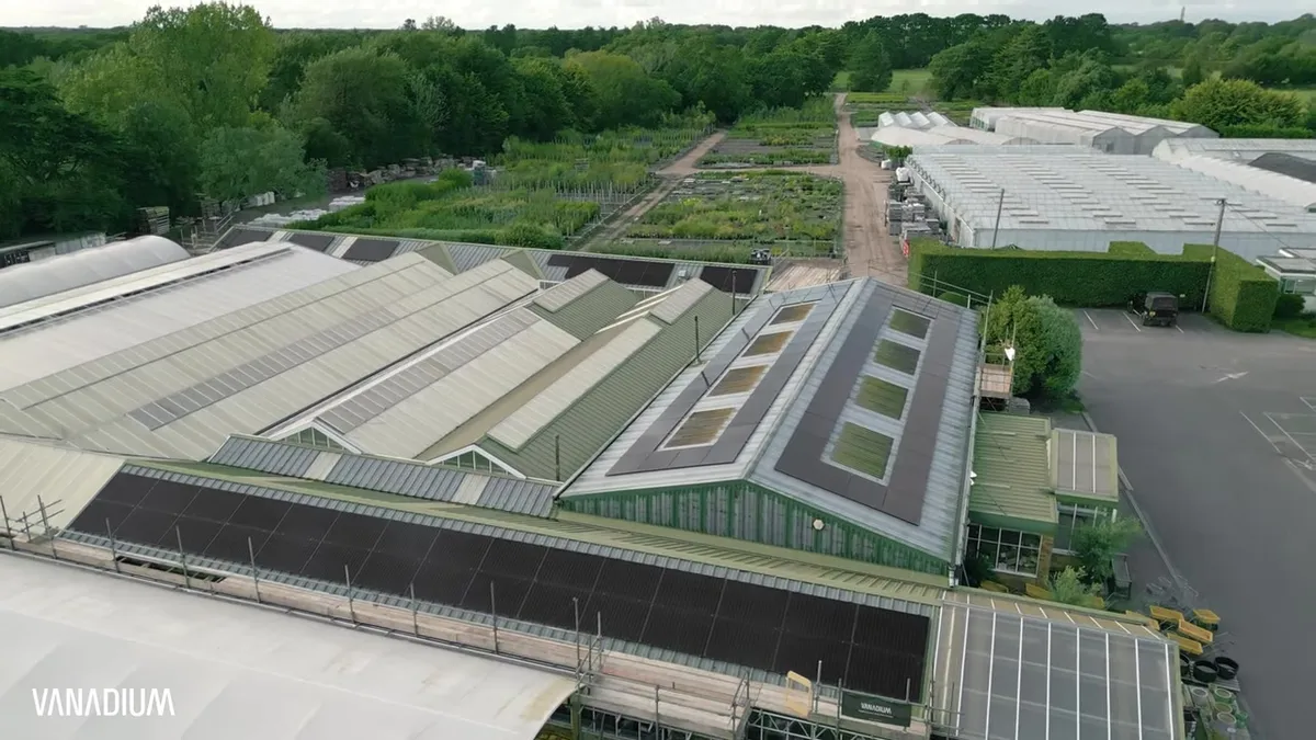 Solar panels are installed on the roofs of multiple large buildings and greenhouses.