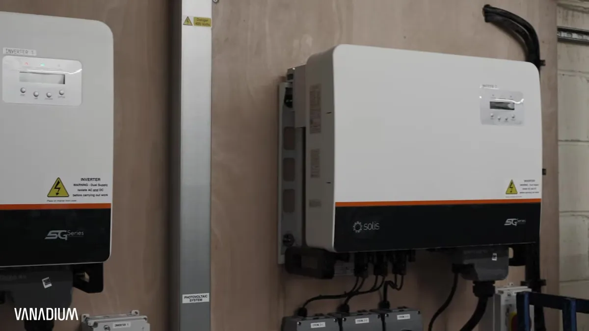 Two large solar inverters are mounted on a wooden wall, with wiring visible below.
