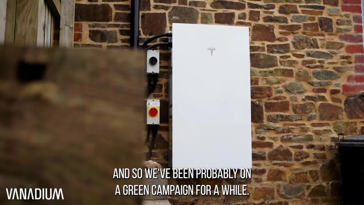 White Tesla Powerwall battery storage unit mounted on a rustic stone wall.