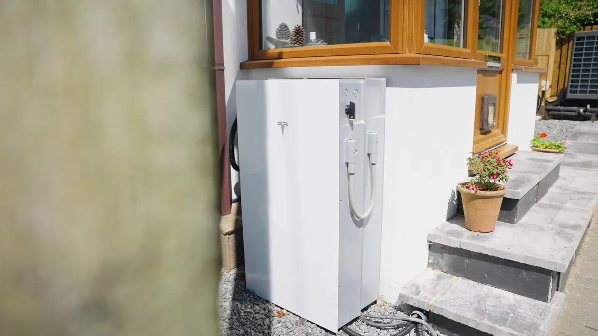 Exterior view of a white Tesla Powerwall battery and an EV charger mounted on the side of a house.