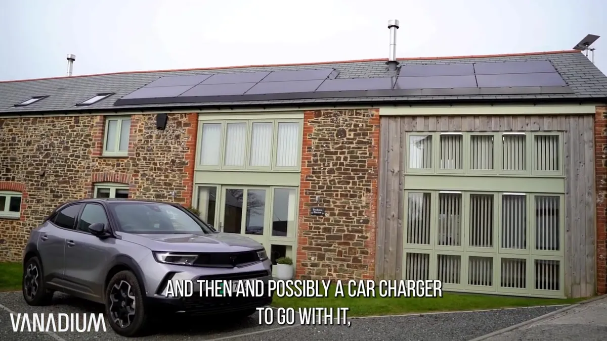 Grey electric car parked in front of a stone barn conversion with solar panels on the roof.