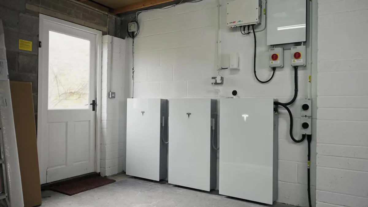 Three Tesla Powerwall batteries are installed in a garage with solar inverters and electrical equipment.