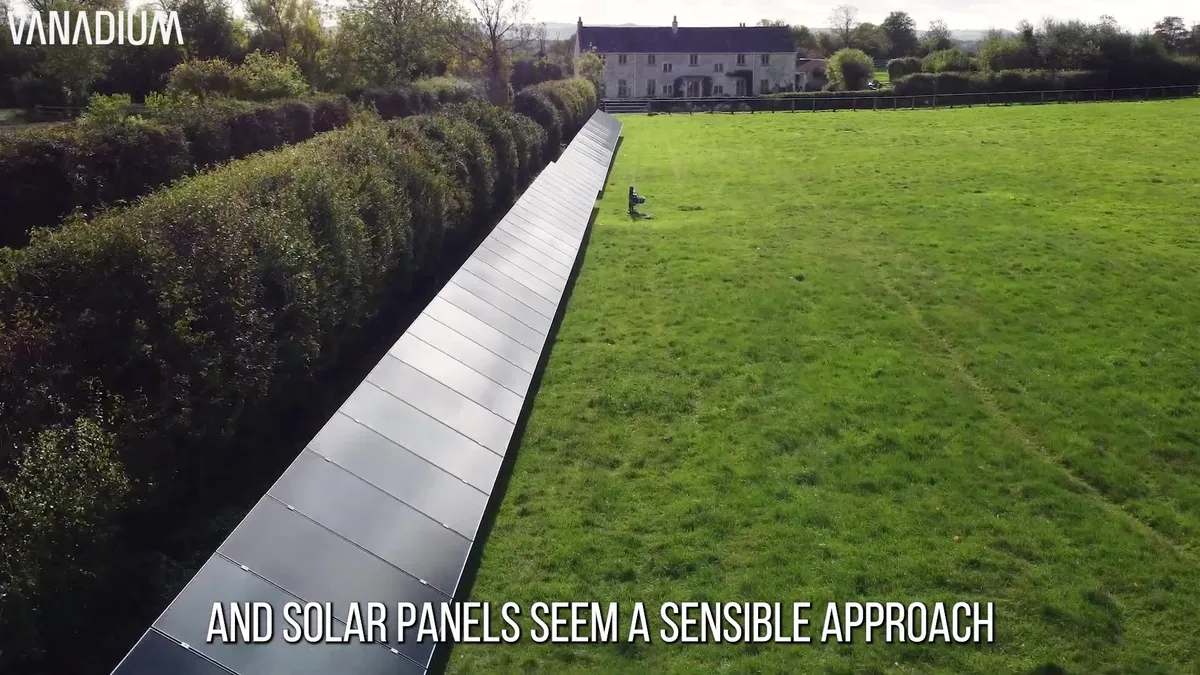 Drone shot showing a long array of ground-mounted solar panels discreetly placed alongside a hedge.