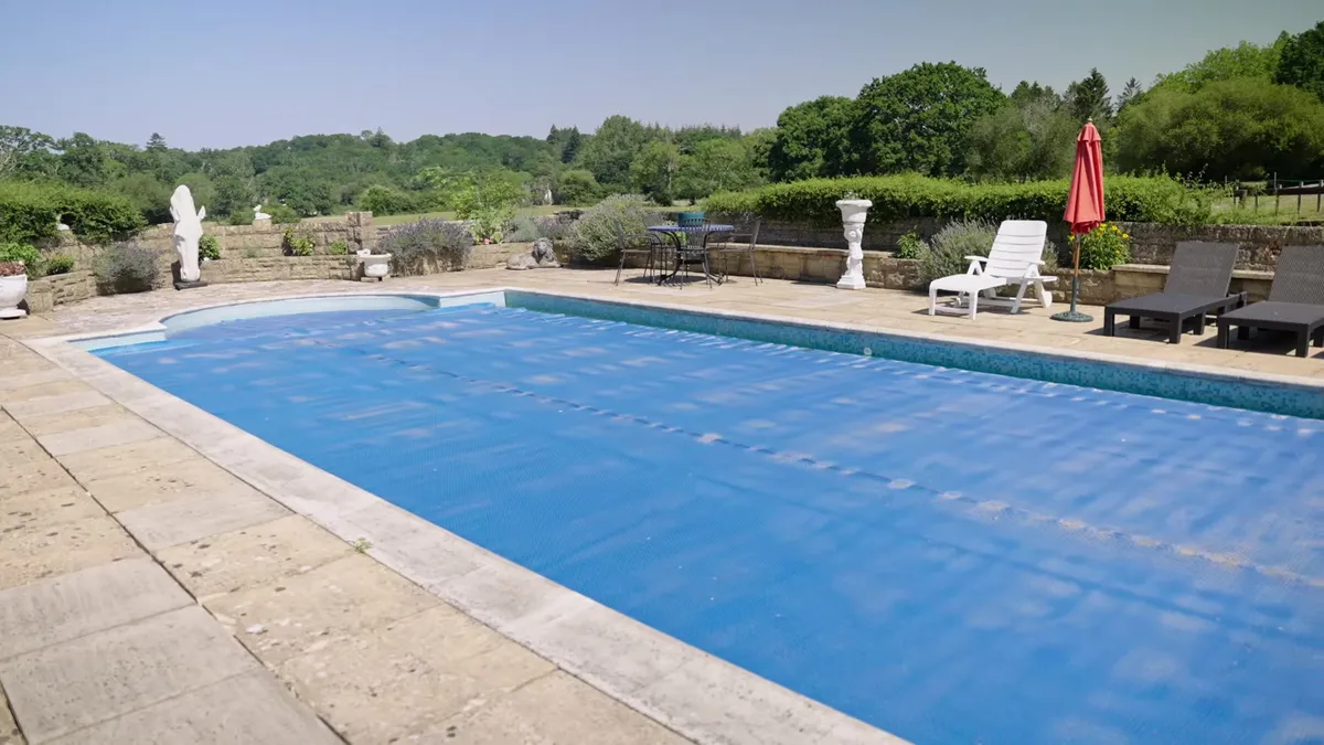 Swimming pool with a blue cover, surrounded by patio and garden.