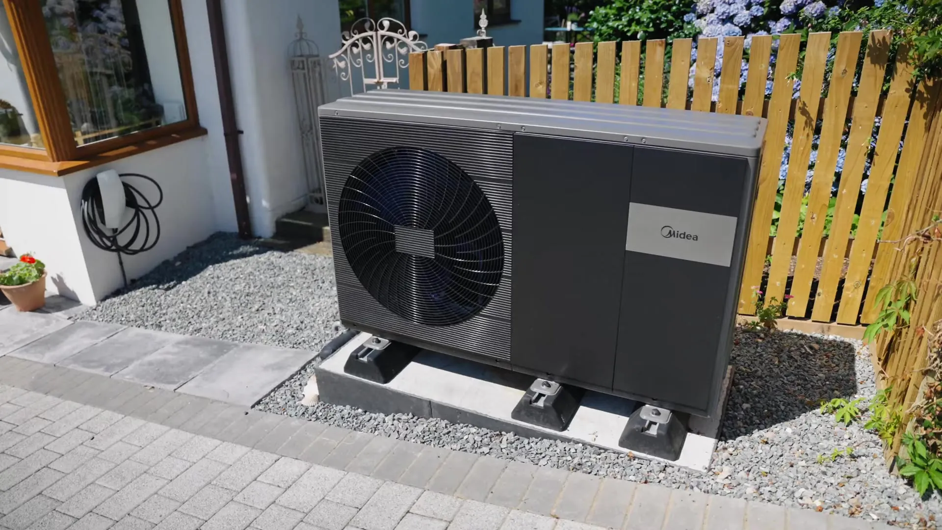 Outdoor unit of a Midea air source heat pump on a gravel bed next to a house.