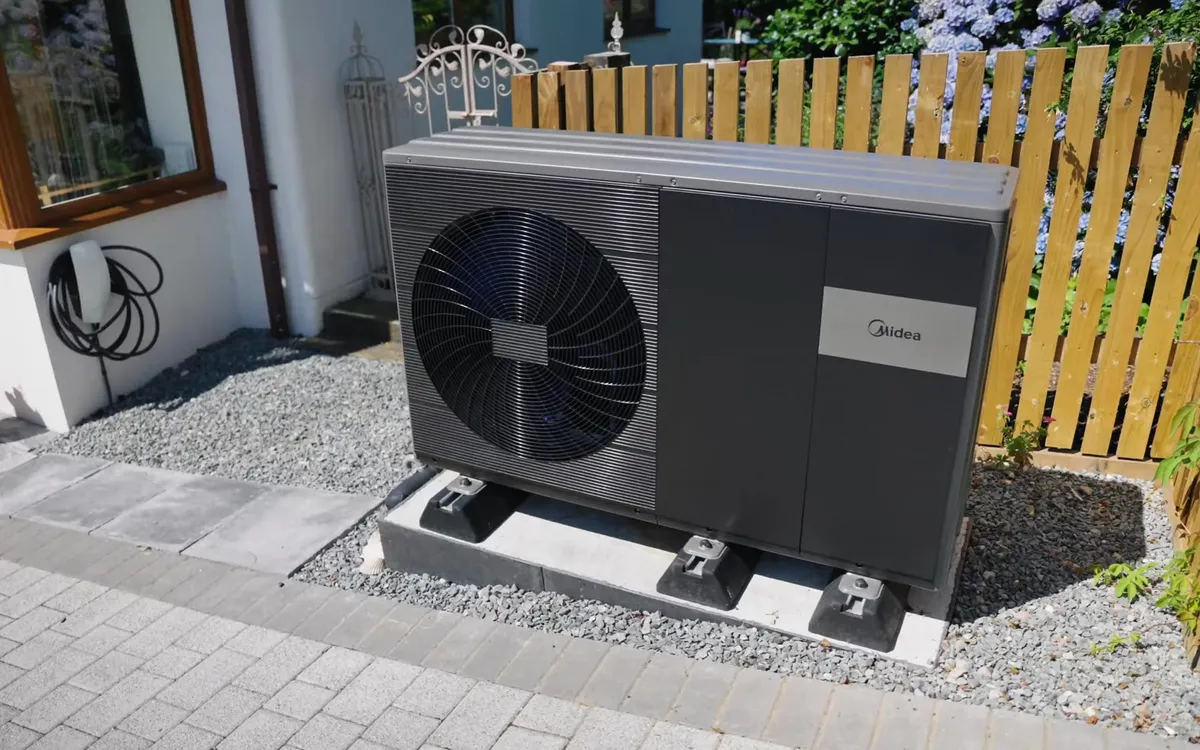 Outdoor unit of a Midea air source heat pump on a gravel bed next to a house.