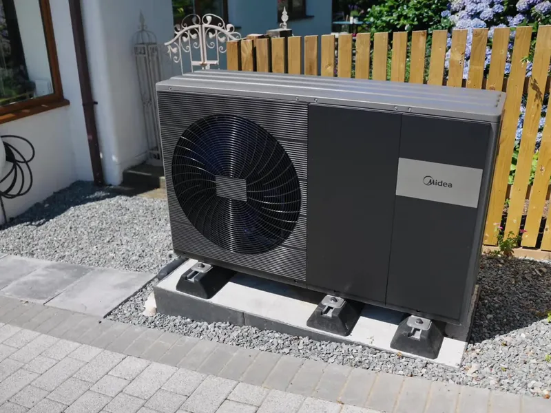 Outdoor unit of a Midea air source heat pump on a gravel bed next to a house.
