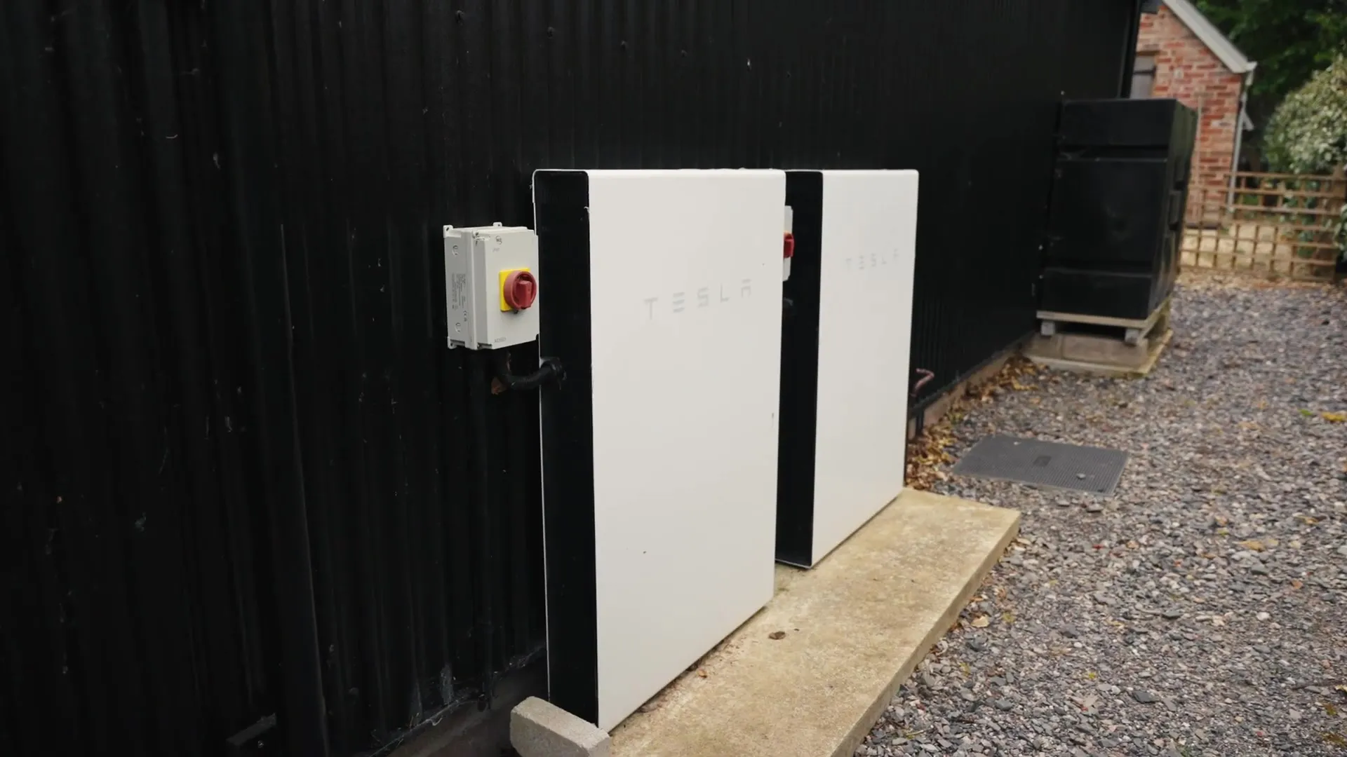 Two white Tesla Powerwall batteries and an isolator switch are installed on a black building.