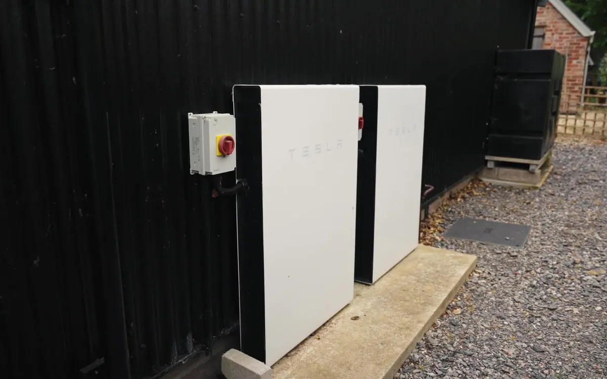 Two white Tesla Powerwall batteries and an isolator switch are installed on a black building.