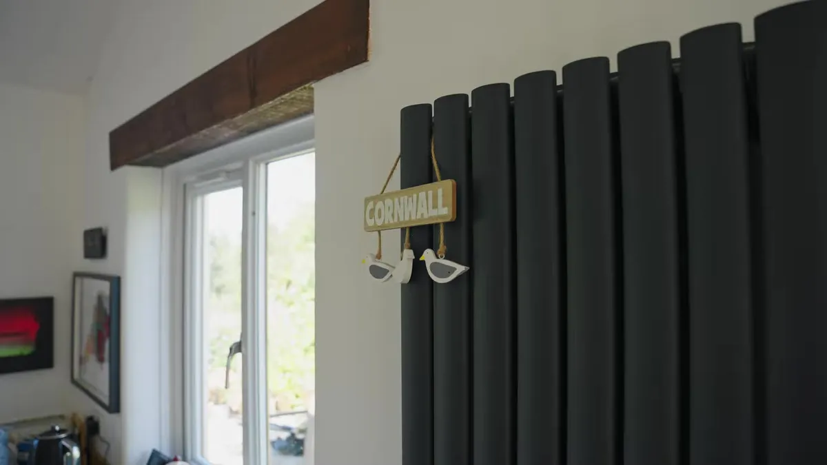 A "Cornwall" sign hangs on a dark grey radiator next to a window.
