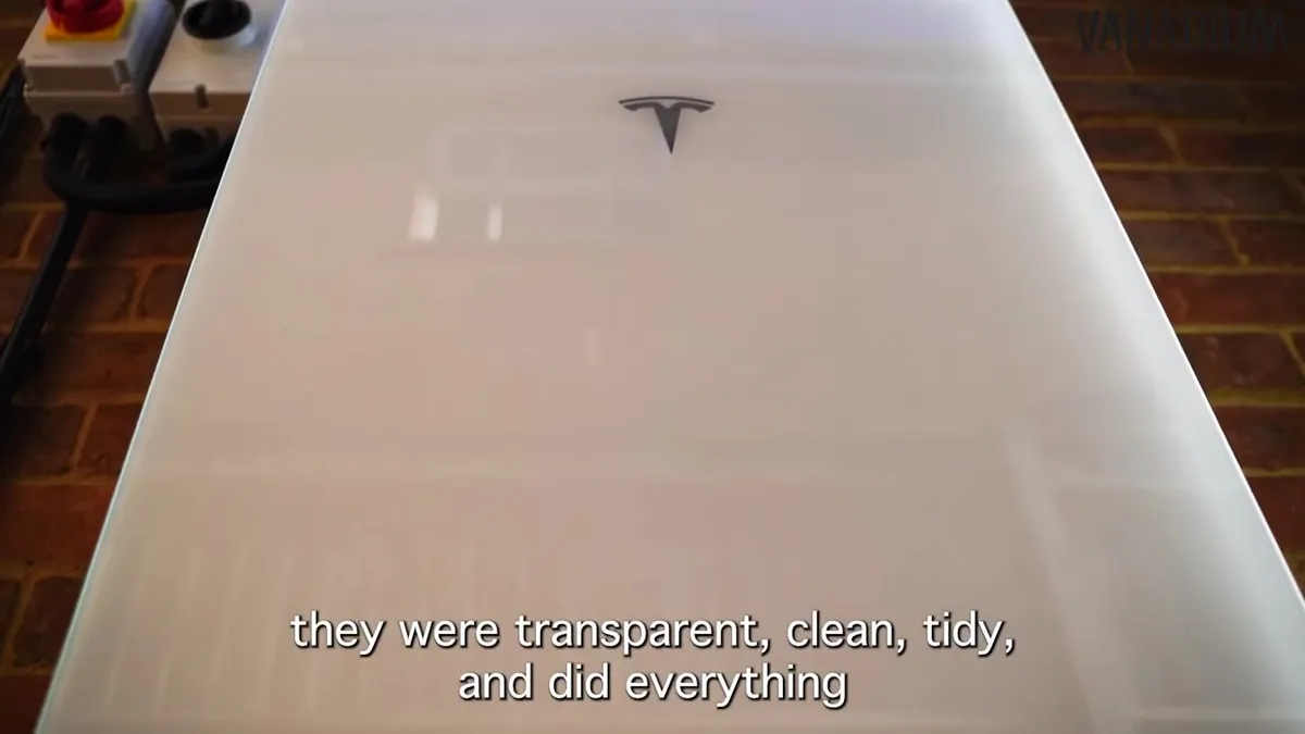 A white Tesla Powerwall 3 battery storage unit mounted on an exterior brick wall of a house.