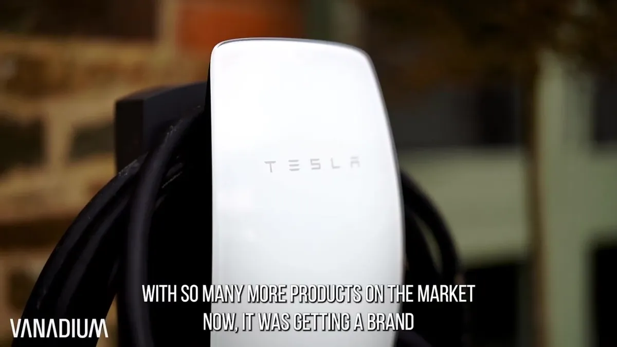 Close-up of a white Tesla Wall Connector EV charger mounted on a stand next to a brick wall.