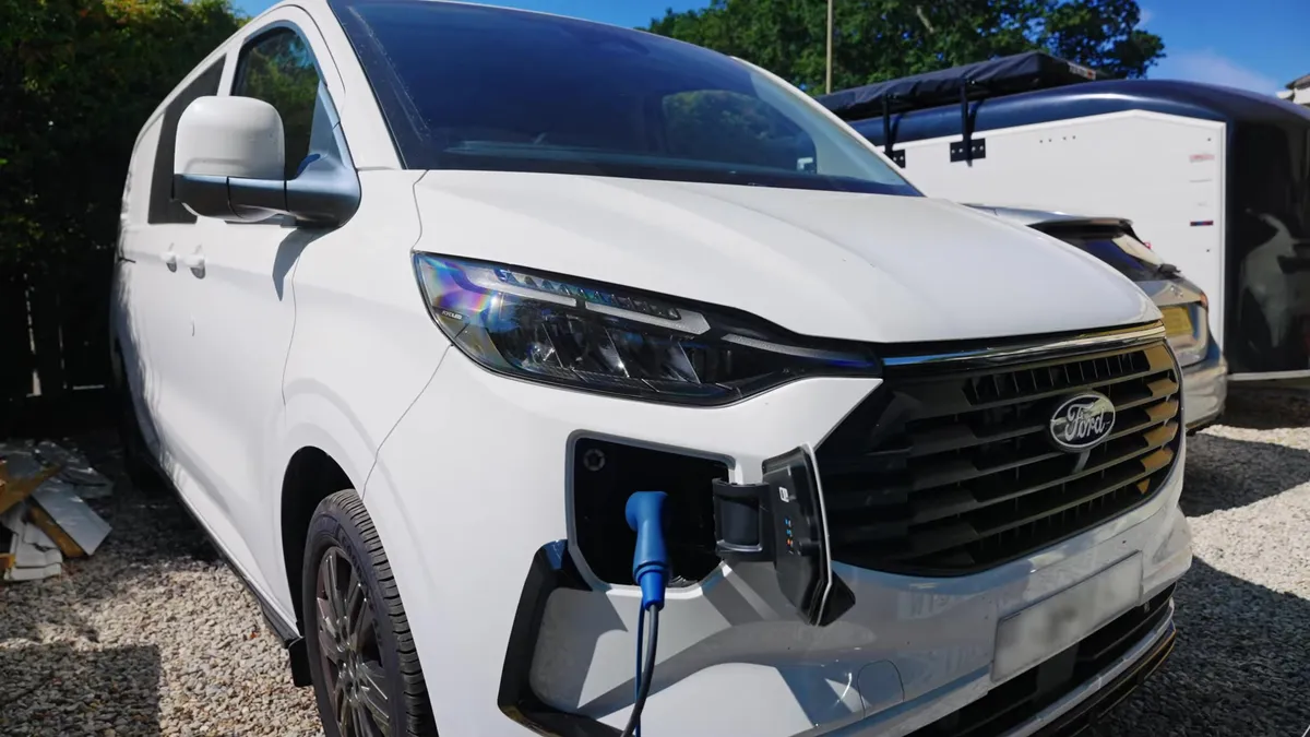 White Ford plug-in hybrid van charging at a home charging station.