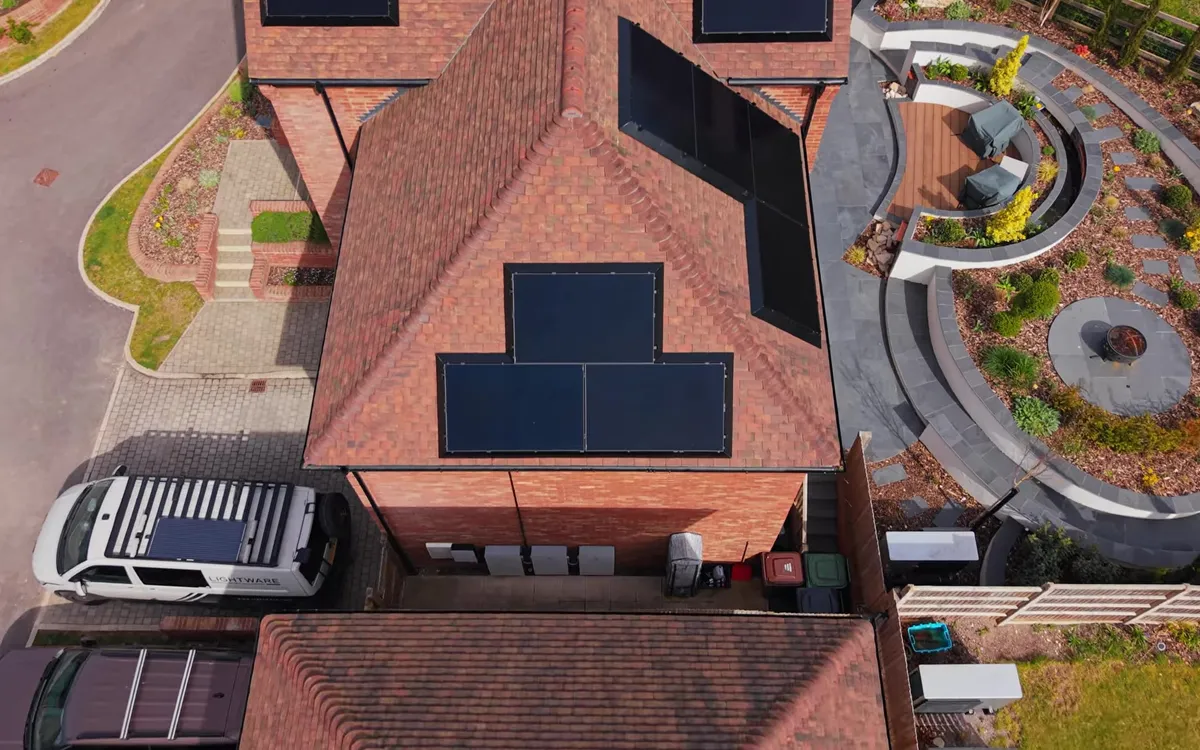 Aerial view of a red brick house with multiple black solar panels on its roof.