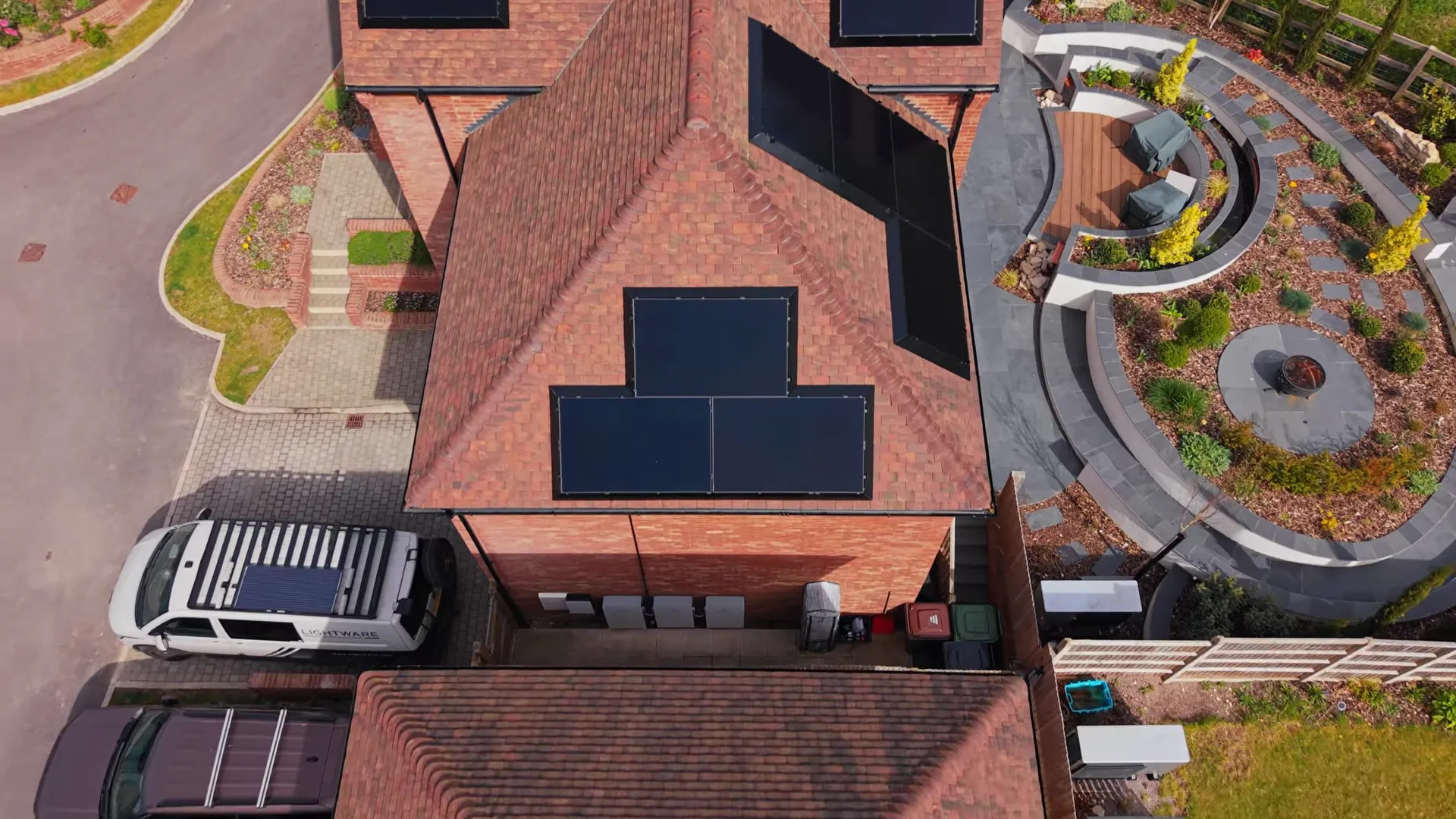 Aerial view of a red brick house with multiple black solar panels on its roof.