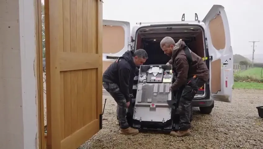 Two Vanadium installers carefully carrying a Tesla Powerwall 3 battery into the garage.