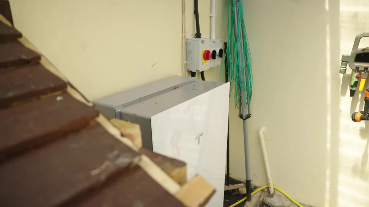 A Tesla Powerwall battery is installed outdoors next to a building.