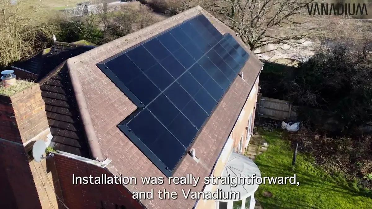 Aerial view of a house with 16 black solar panels neatly installed on its brown tiled roof.